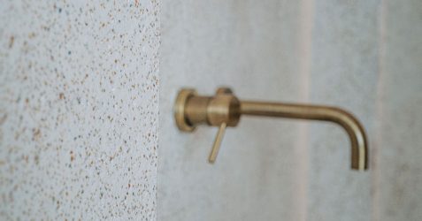 Close-up detail of microtopping in bathroom wall showing speckled texture finish with mounted brass faucet fixture